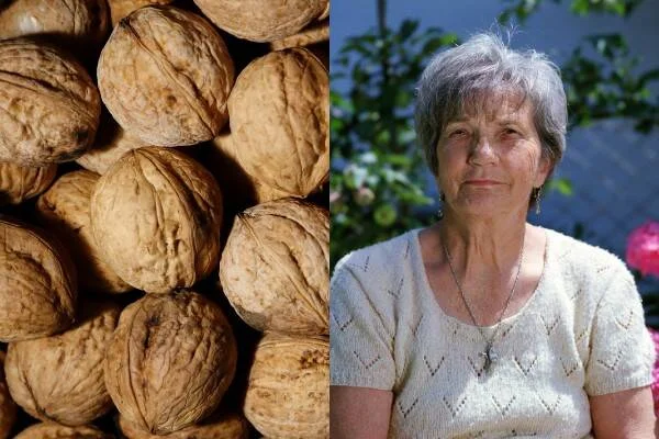 Montón de nueces con cáscara junto al retrato de una mujer mayor de cabello canoso en un jardín.