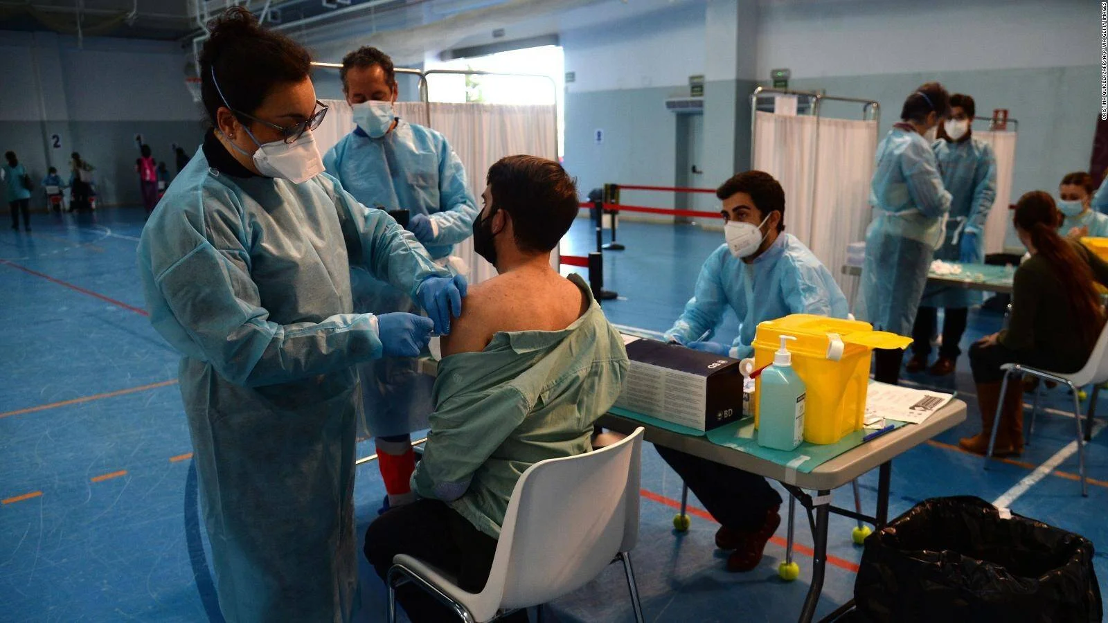 Personal sanitario con equipo de protección aplica una vacuna en el brazo a un hombre en un centro de vacunación masiva.