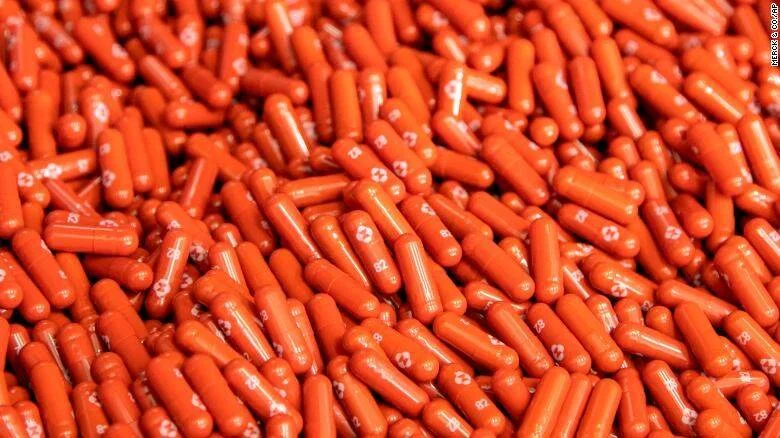 Gran cantidad de cápsulas farmacéuticas de color naranja con marcas impresas, apiladas en masa.
