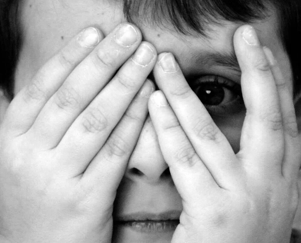 Niño se cubre el rostro con ambas manos, dejando un ojo visible, en expresión de miedo o angustia.