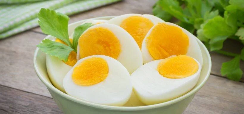 Tazón con huevos duros cortados por la mitad, mostrando yema amarilla, decorados con perejil fresco.
