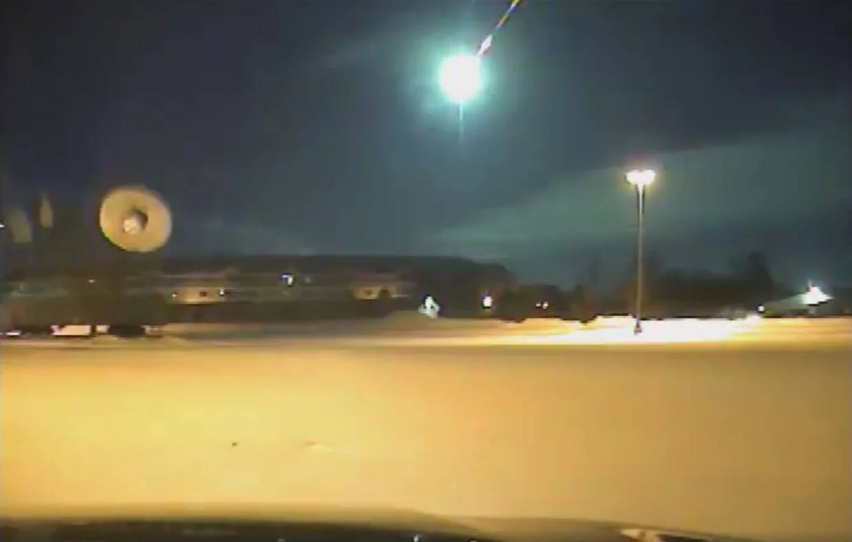 Un brillante meteoro verde ilumina el cielo nocturno sobre una zona urbana nevada, captado por una cámara de seguridad.