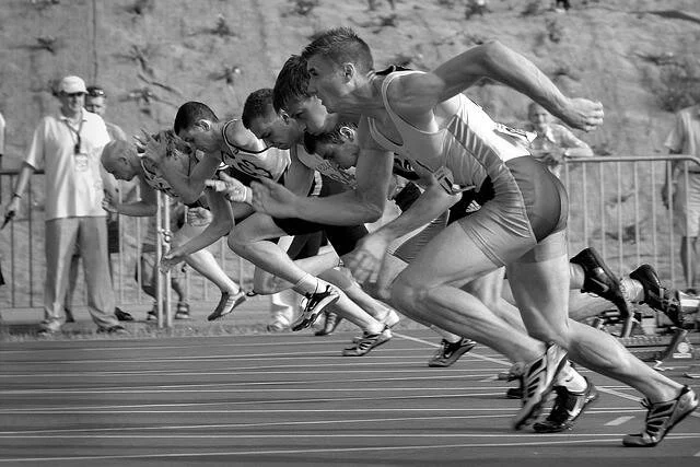 Grupo de velocistas arrancando desde los tacos de salida en una competencia de atletismo en pista.