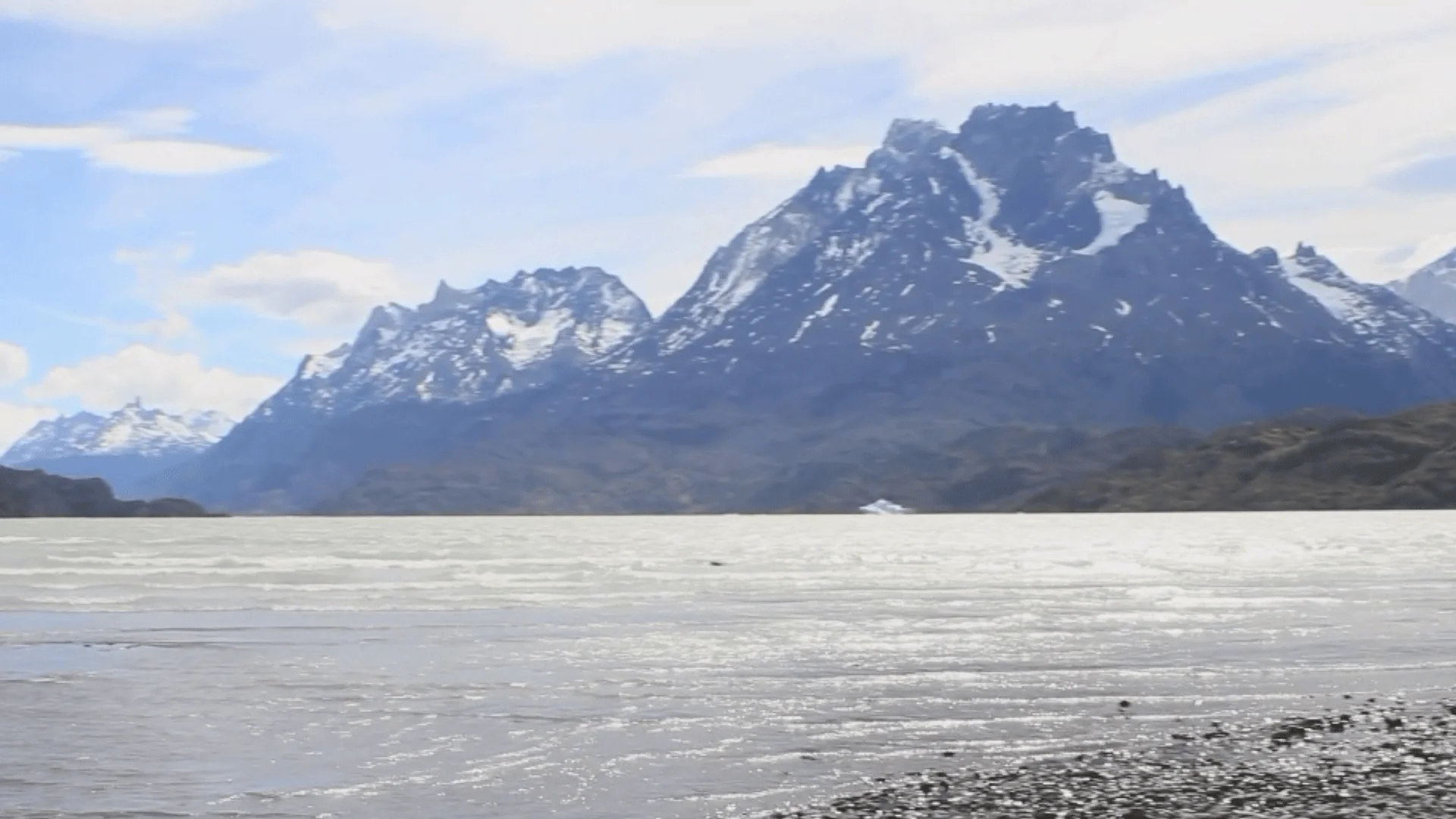 Lago de aguas grises con bloques de hielo frente a imponentes picos montañosos con nieve en la Patagonia.