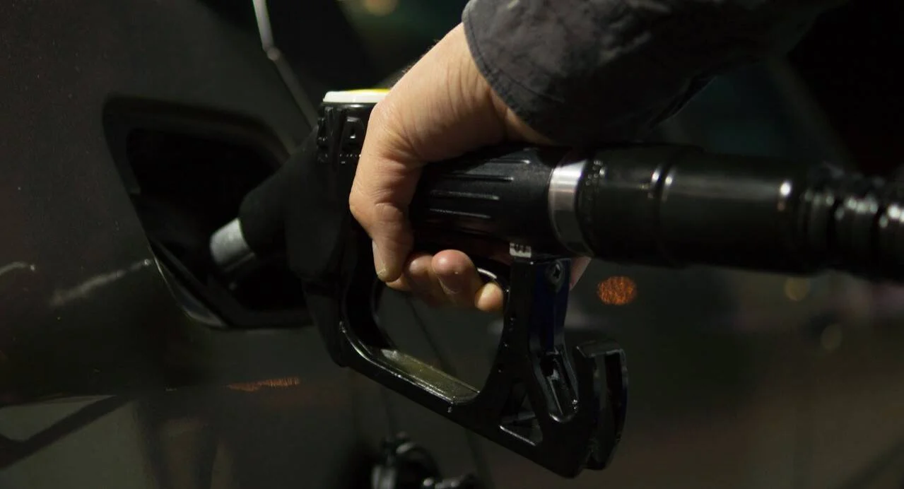 Una mano introduce la pistola surtidora de combustible en el tanque de un vehículo en una estación de servicio.