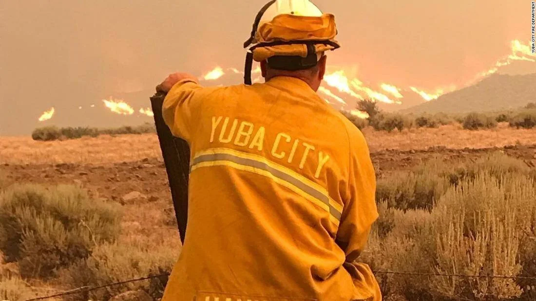 Bombero del Departamento de Yuba City observa las llamas avanzando sobre vegetación árida en un incendio forestal.