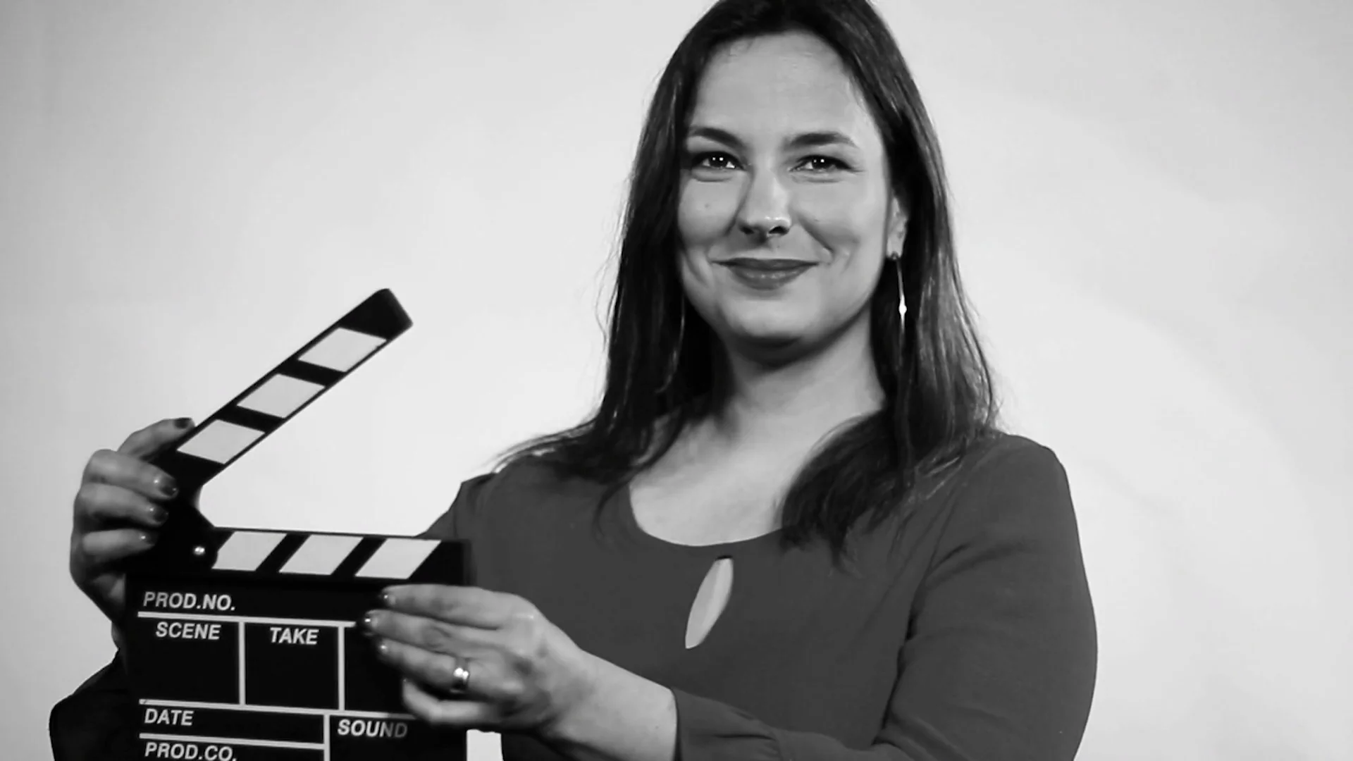 Mujer sonriente sostiene una claqueta de filmación en una fotografía en blanco y negro.