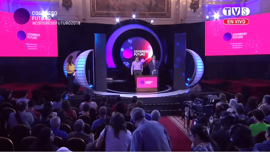 Dos presentadores en el escenario del Congreso Futuro 2018, transmitido en vivo por TVS, ante un auditorio lleno de público.