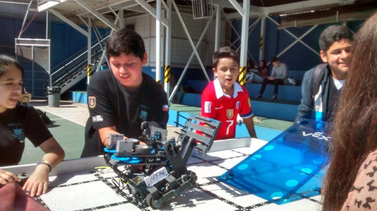 Jóvenes estudiantes manipulan un robot VEX sobre una pista de competencia durante un torneo de robótica escolar.