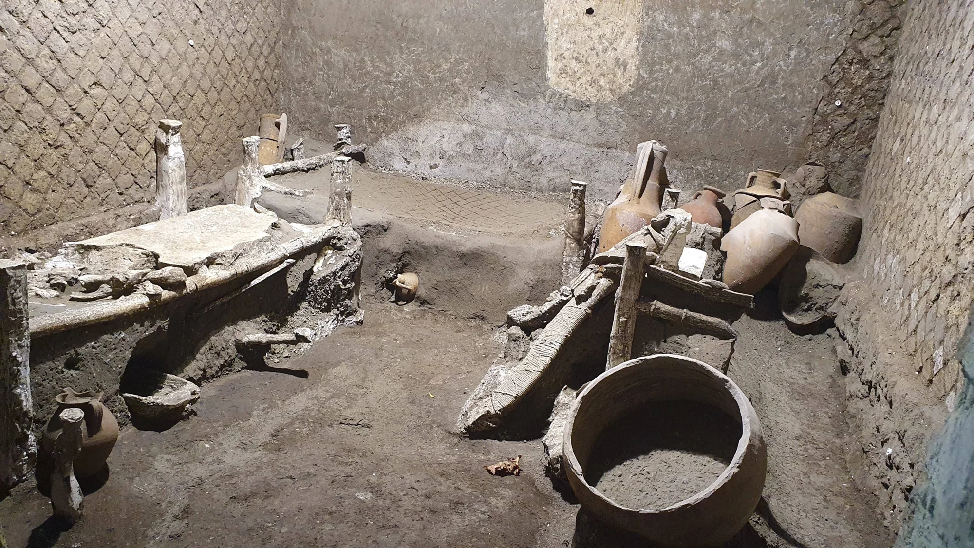 Interior de una habitación arqueológica con ánforas, restos de madera carbonizada y objetos de cerámica cubiertos de ceniza volcánica.