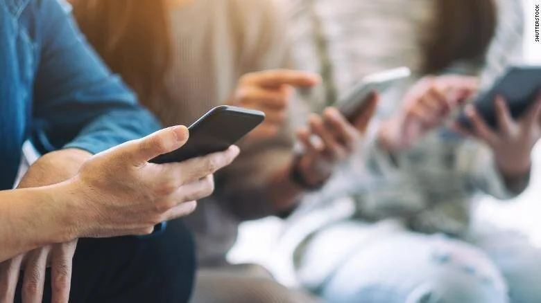 Varias personas sentadas una junto a otra utilizando sus teléfonos inteligentes simultáneamente.