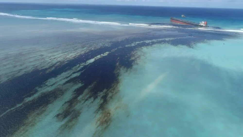 Vista aérea de una gran mancha de petróleo extendiéndose en el océano desde un buque de carga encallado en un arrecife de coral.