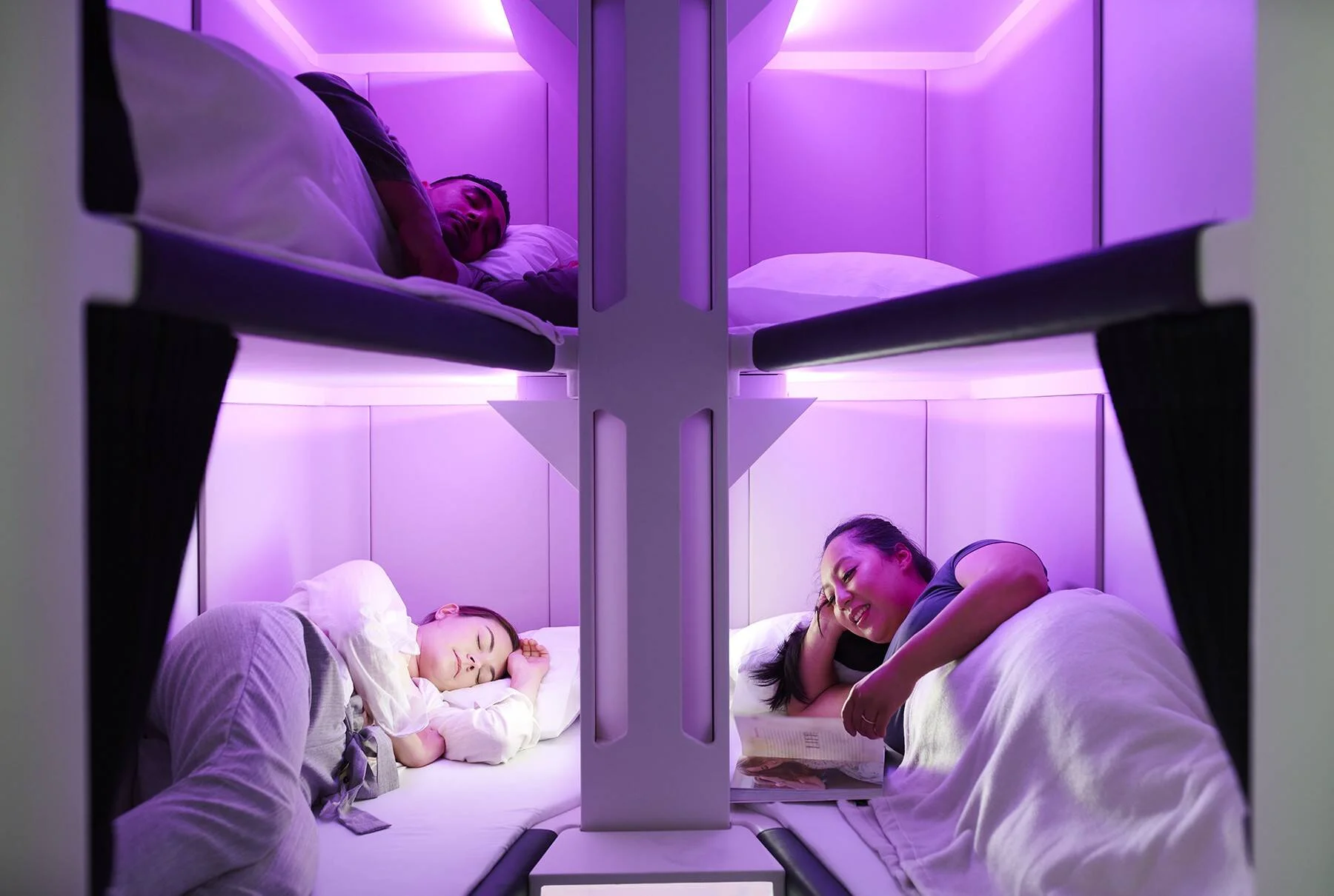 Tres pasajeros descansan en literas iluminadas con luz violeta dentro de una cabina de avión, dos durmiendo y uno leyendo.