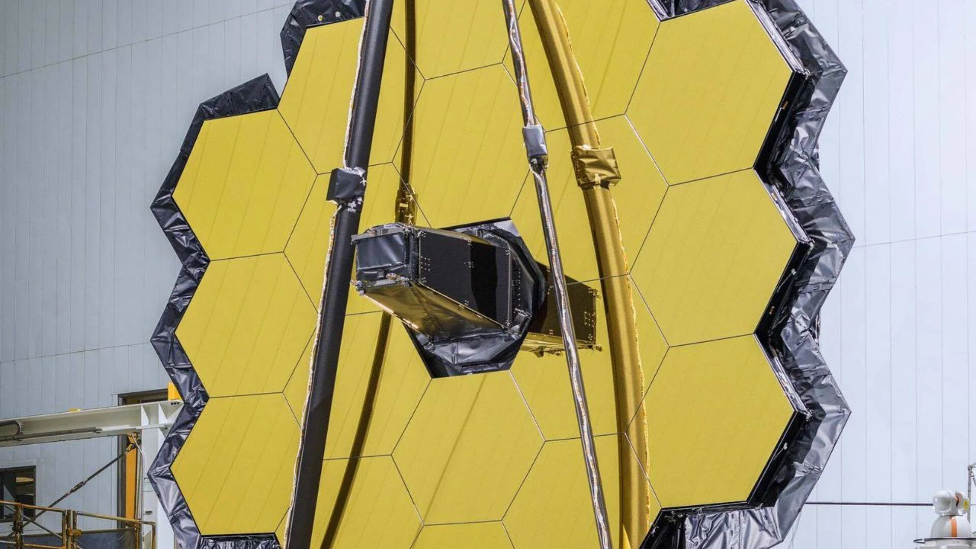 Espejo primario de un telescopio espacial compuesto por segmentos hexagonales bañados en oro, montado en instalación de ensamblaje.