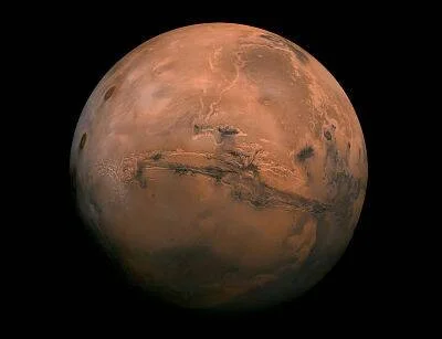 El planeta Marte visto desde el espacio, mostrando su superficie rojiza con cañones y cráteres sobre fondo negro.