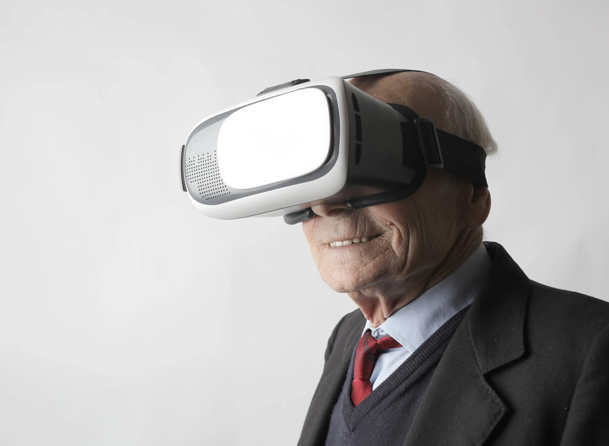 Hombre mayor con traje y corbata roja sonríe mientras usa un casco de realidad virtual.