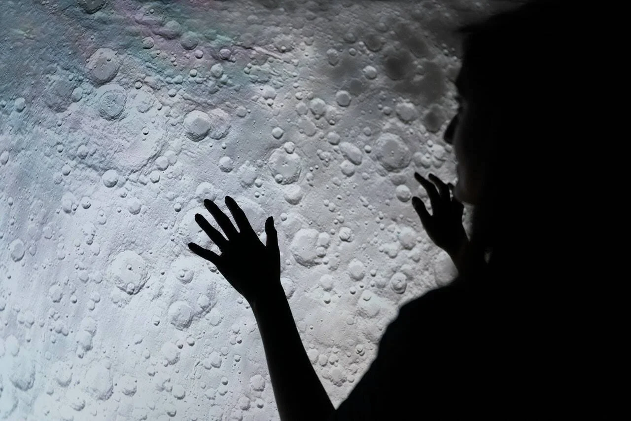 Silueta de una persona con las manos extendidas sobre una proyección de la superficie lunar con cráteres.