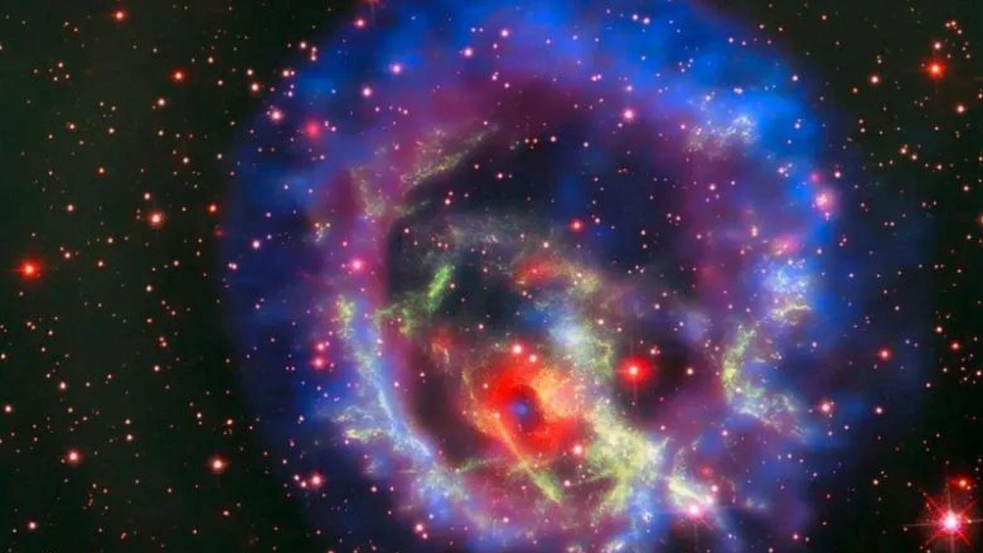 Remanente de supernova con nubes de gas en tonos azul, rojo y verde rodeado de estrellas en el espacio profundo.