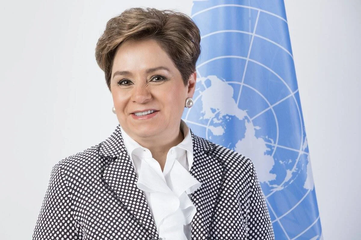 Mujer con saco a lunares sonríe frente a la bandera de las Naciones Unidas en una foto oficial.