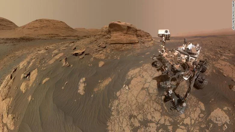 El rover Curiosity de la NASA se fotografía a sí mismo sobre el suelo rocoso de Marte, con formaciones geológicas estratificadas al fondo.
