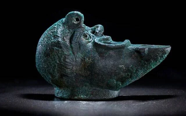 Pequeña escultura de bronce antiguo con pátina verde, que representa una cabeza de animal con boca abierta.