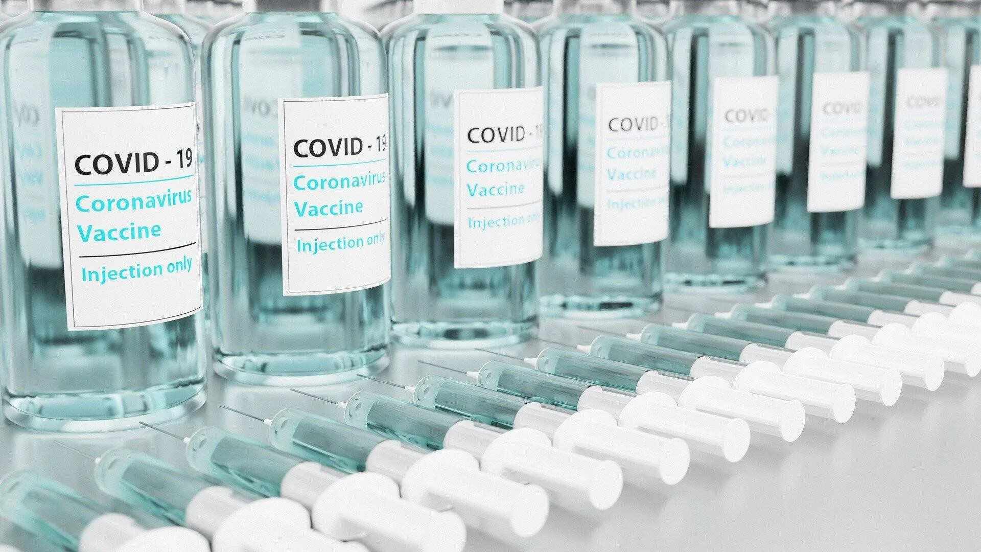 Fila de frascos de vidrio etiquetados como vacuna contra el COVID-19 junto a jeringas listas para su aplicación.