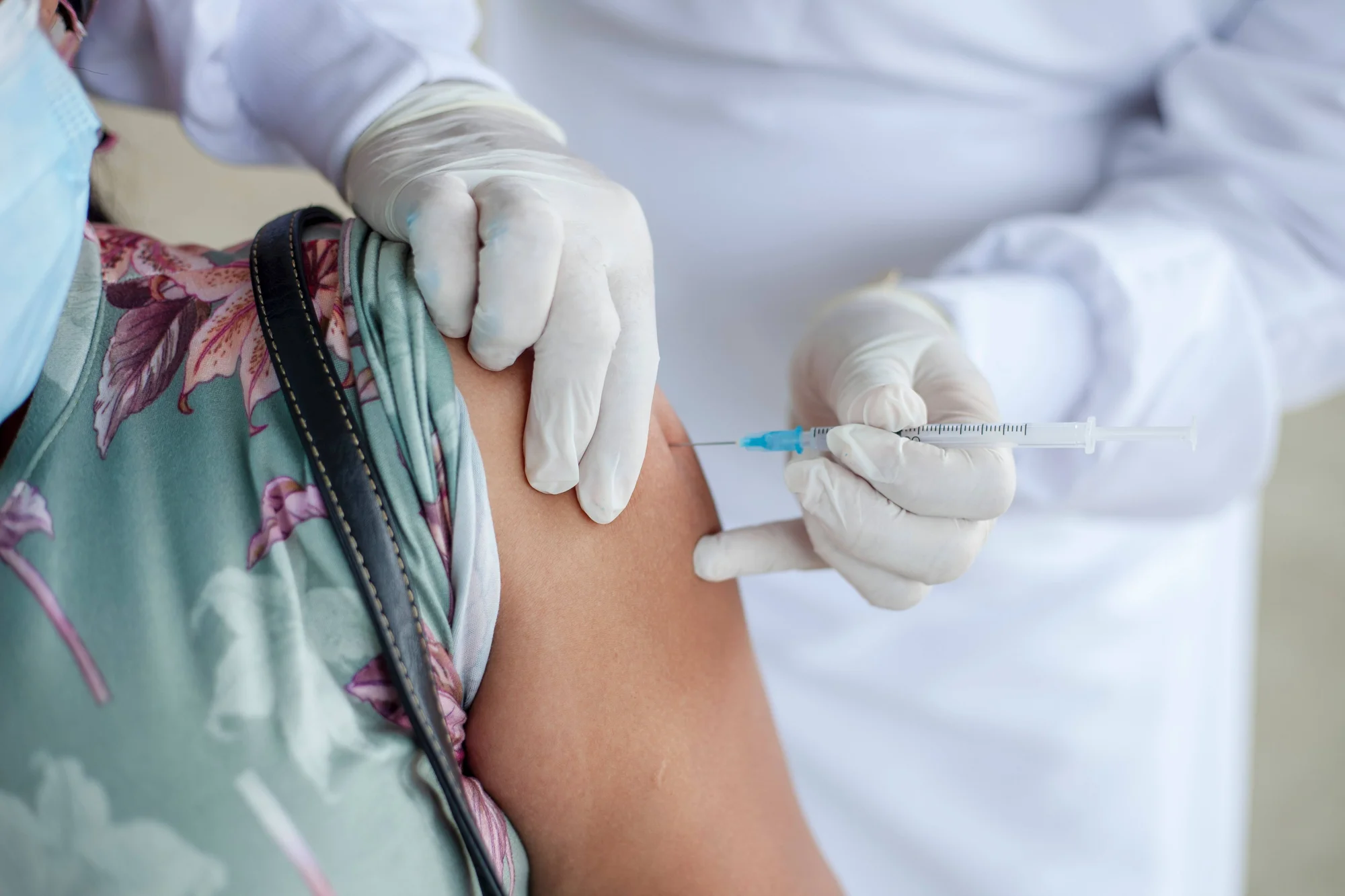 Un profesional sanitario con guantes aplica una inyección en el brazo de una persona con mascarilla.