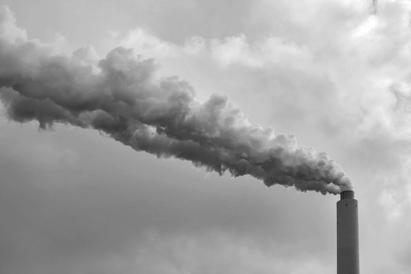 Chimenea industrial expulsando una densa columna de humo que se expande horizontalmente en un cielo nublado.
