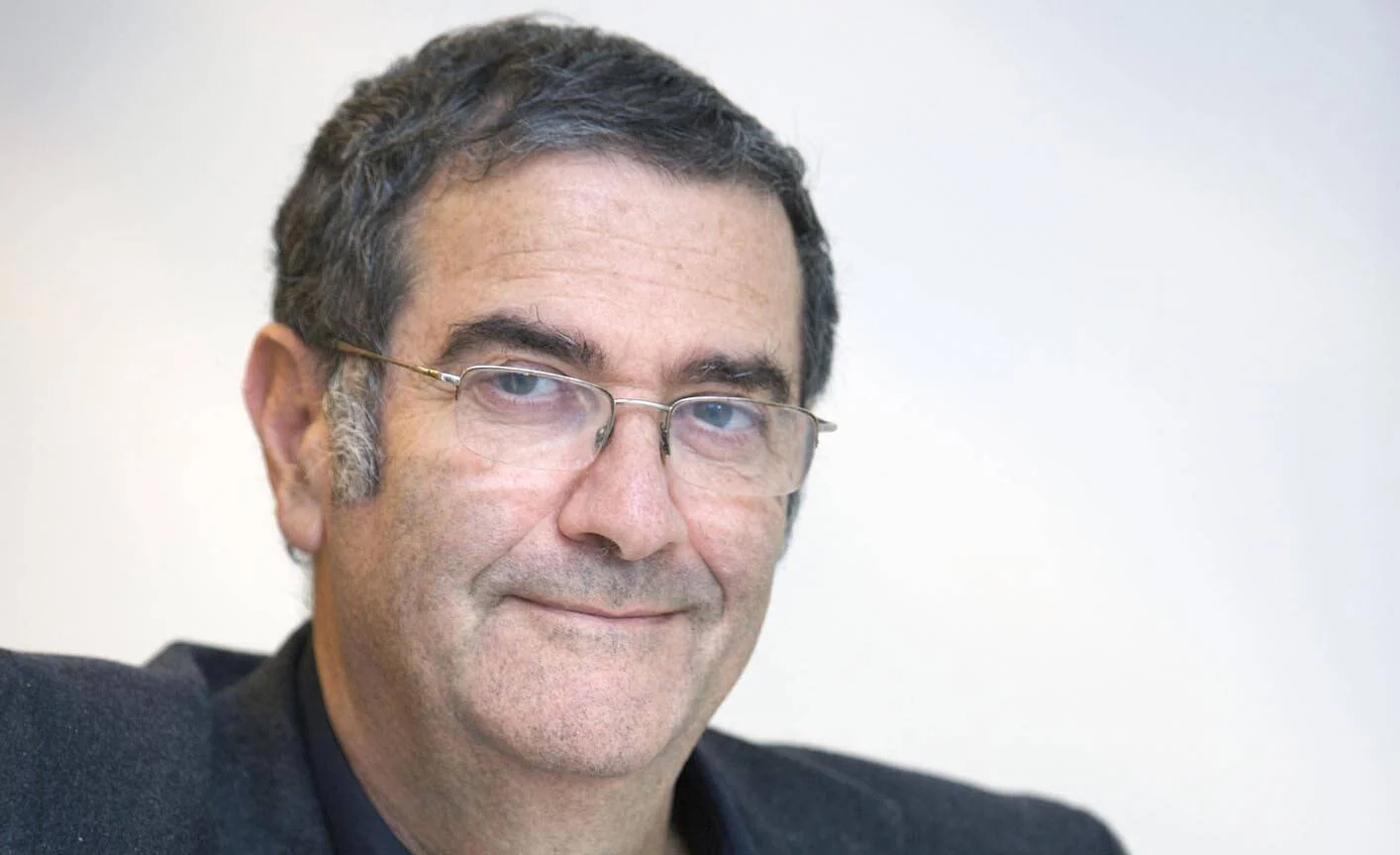 Hombre de mediana edad con cabello oscuro entrecano, gafas de montura metálica y ropa negra, con expresión serena.