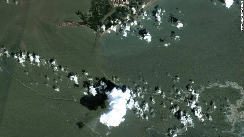 Vista satelital de una región costera con extensas inundaciones y nubes dispersas sobre campos y localidad ribereña.