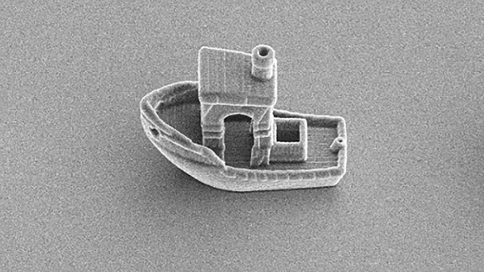 Imagen de microscopio electrónico de barrido muestra un diminuto barco impreso en 3D a nanoescala con detalles de cabina y chimenea.