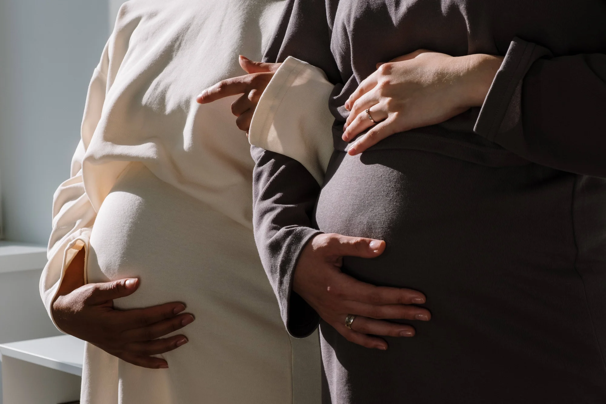 Dos mujeres embarazadas, de pie una junto a la otra, sostienen sus vientres con las manos.