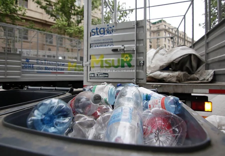 Contenedor lleno de botellas plásticas aplastadas frente a camión de reciclaje del Gobierno Regional Metropolitano de Santiago.