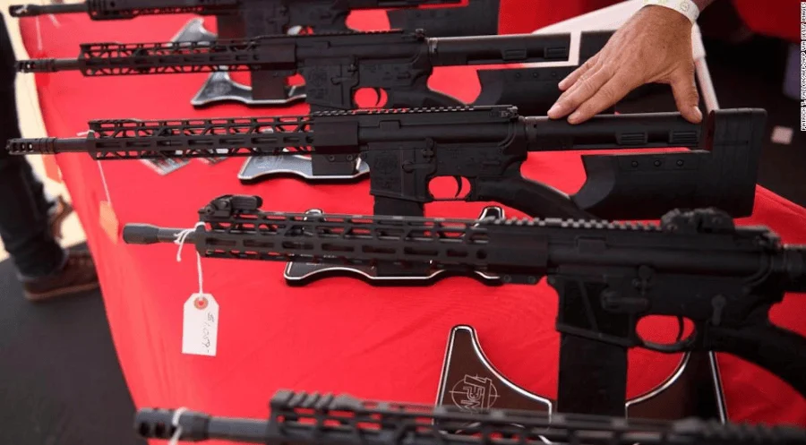 Varios rifles semiautomáticos negros exhibidos sobre una mesa con mantel rojo, con una mano sosteniendo uno de ellos.