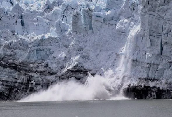 Un bloque de hielo se desprende de un glaciar y cae al agua, generando una nube de vapor y salpicaduras.