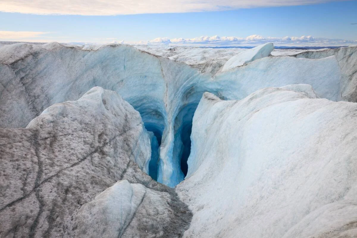 Profunda fisura de hielo azul en la superficie de un glaciar, con el casquete helado extendiéndose hasta el horizonte.