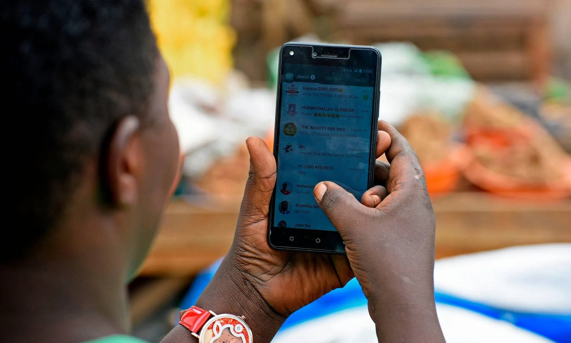 Una persona sostiene un teléfono móvil mostrando una lista de chats de WhatsApp en un entorno al aire libre.