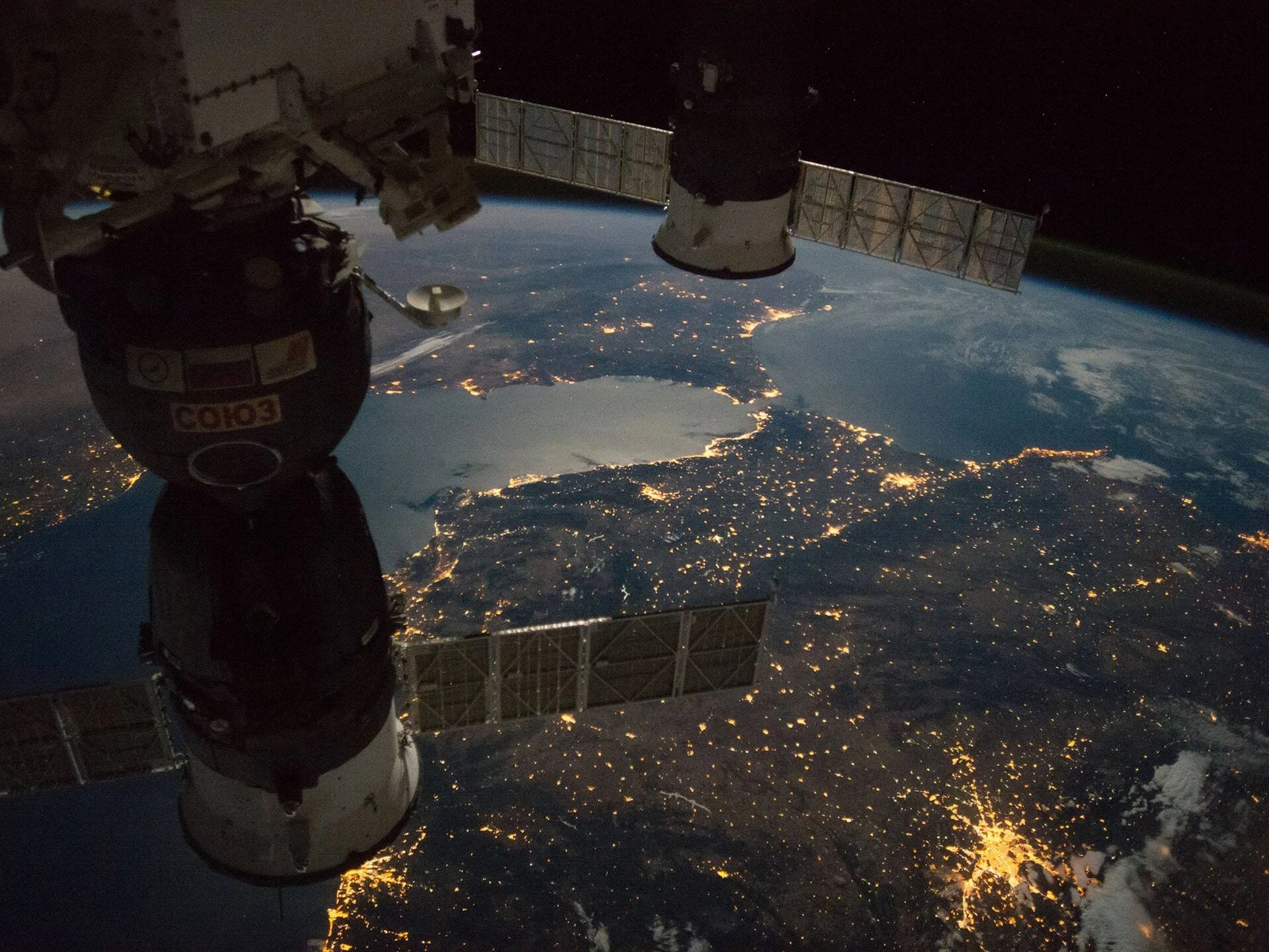 Cápsula Soyuz acoplada a la EEI con luces de ciudades terrestres visibles de noche desde el espacio.