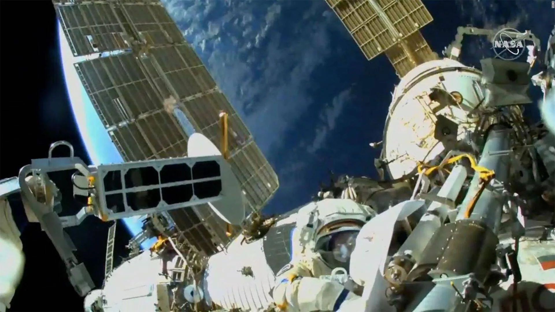 Astronauta con traje espacial realizando una caminata extravehicular en el exterior de la Estación Espacial Internacional, con la Tierra de fondo.