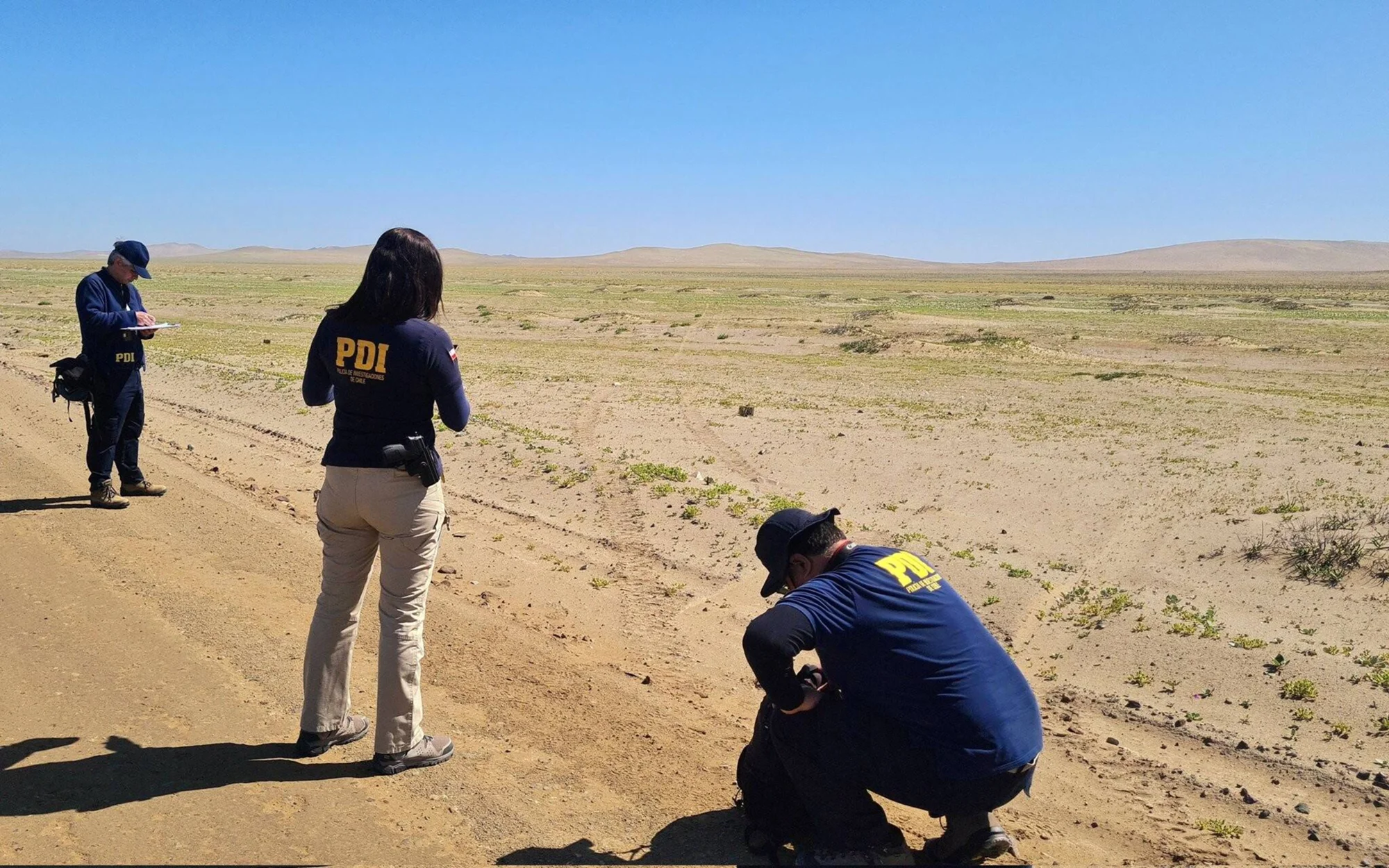 Tres agentes de la PDI de Chile realizan labores de investigación en un camino de tierra en el desierto.