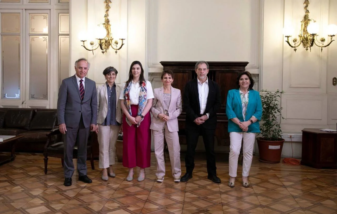 Seis funcionarios posan juntos en un salón de estilo clásico con apliques dorados y piso de parquet.