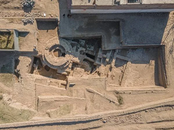 Vista cenital de un sitio arqueológico en excavación con muros y estructuras circulares de piedra al descubierto.