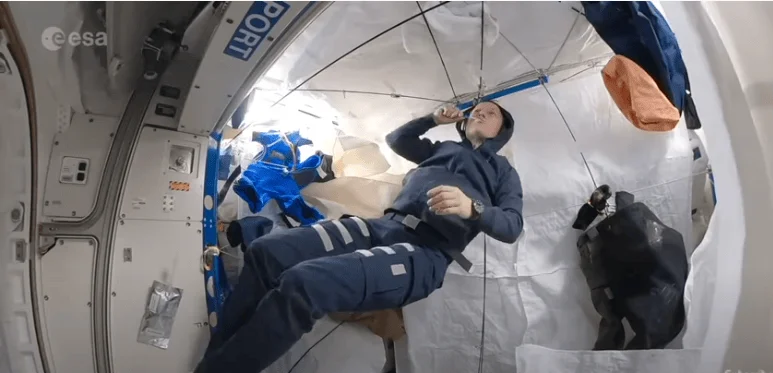 Astronauta de la ESA en ingravidez dentro de un módulo de la Estación Espacial Internacional, con objetos flotando a su alrededor.