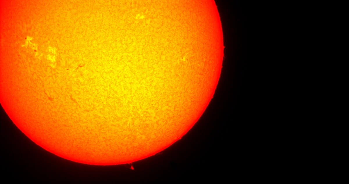 Fotografía telescópica del Sol mostrando su superficie granulada en tonos naranja y amarillo, con una pequeña prominencia solar en el borde inferior.
