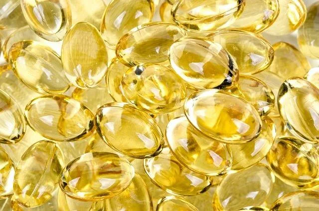 Múltiples cápsulas de gel amarillo dorado de aceite de pescado o vitamina D apiladas en primer plano.