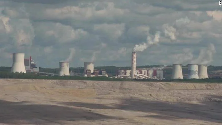 Planta de energía de carbón con múltiples torres de enfriamiento emitiendo vapor, vista desde una mina a cielo abierto.