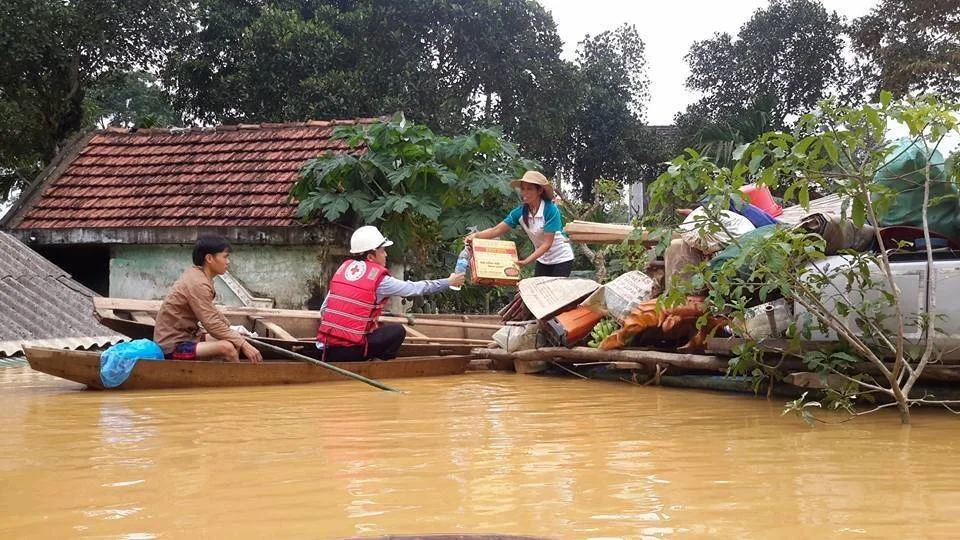 Voluntario de la Cruz Roja en bote entrega paquete de ayuda a afectados por inundación en zona rural anegada.