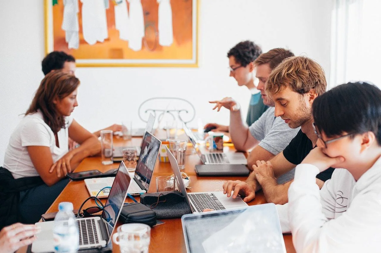 Grupo de personas trabajando con laptops alrededor de una mesa en una reunión de equipo.