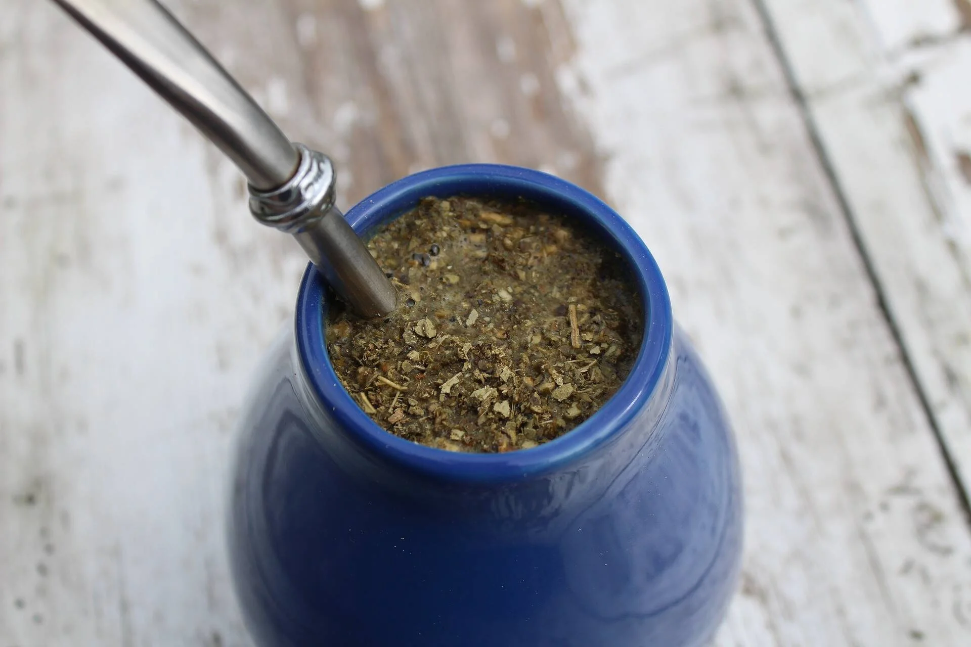 Mate de cerámica azul con yerba cebada y bombilla de metal, visto desde arriba sobre superficie de madera.