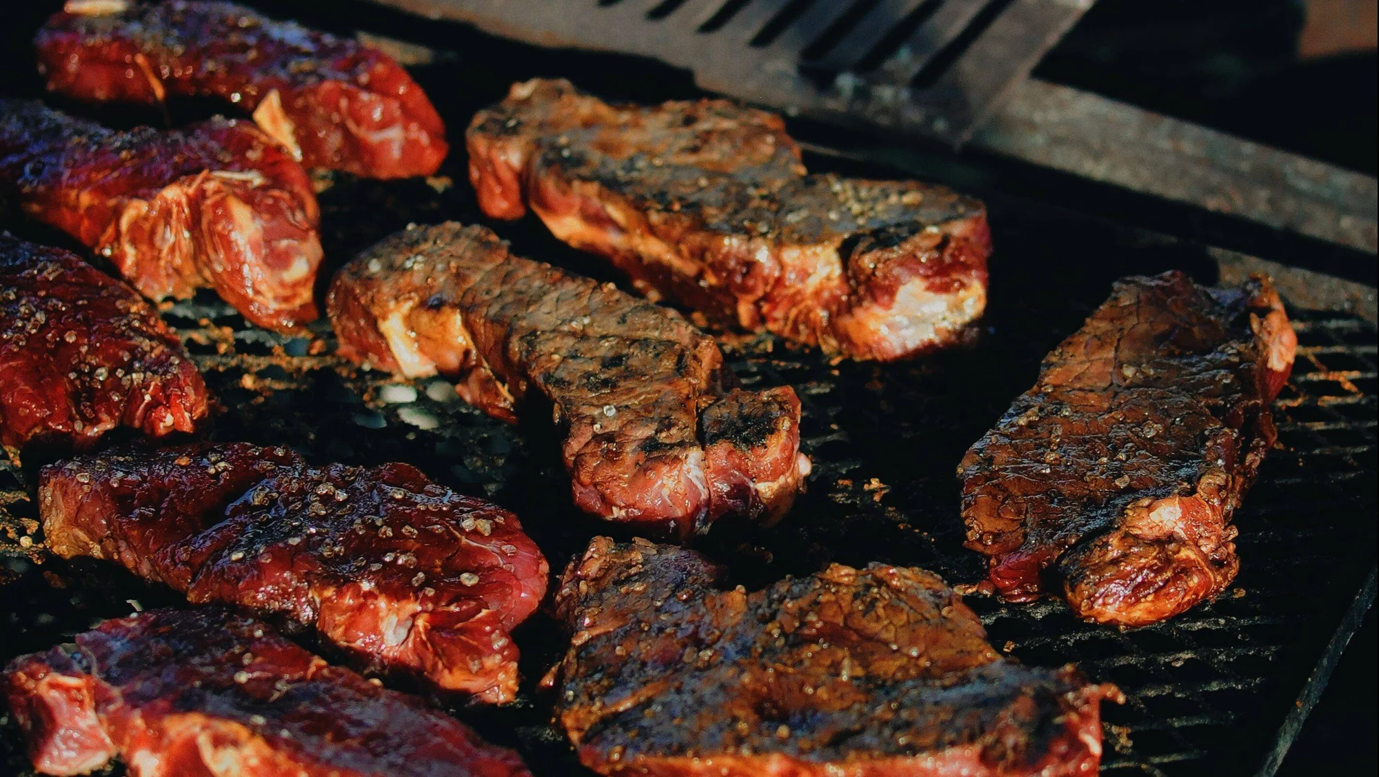 Varios cortes de carne sazonados cocinándose sobre una parrilla caliente con marcas de brasa.